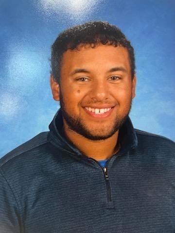 A young man in a blue sweater is smiling for a picture.