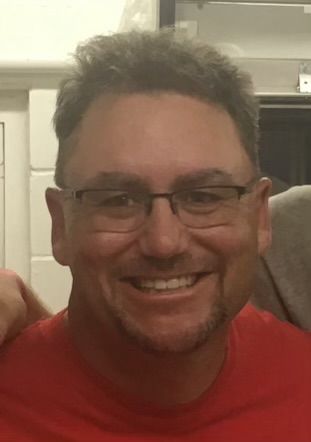 A man wearing glasses and a red shirt is smiling for the camera. This is Dan Kirby.