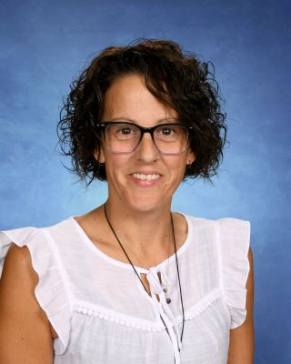 A woman wearing glasses and a white shirt is smiling for the camera.