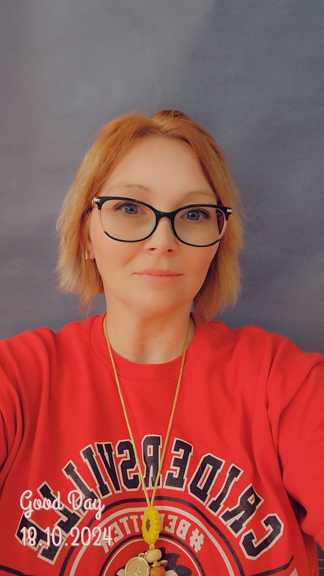 A woman wearing glasses and a red shirt is taking a selfie.