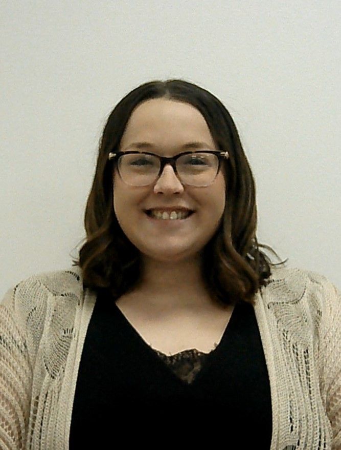 A woman wearing glasses and a sweater is smiling for the camera. This is Kelsi Kuprat.