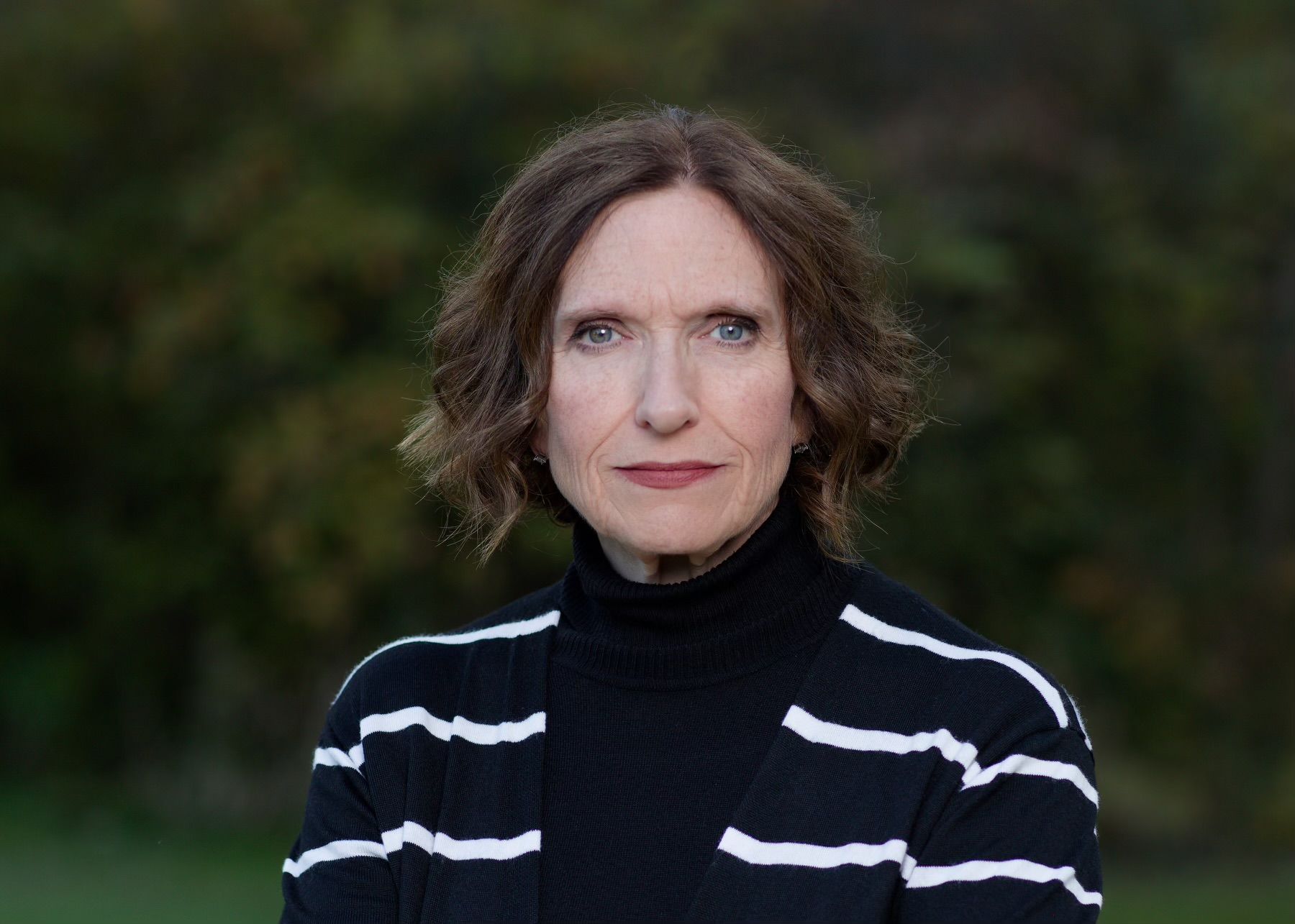 A woman is wearing a black and white striped sweater and looking at the camera.