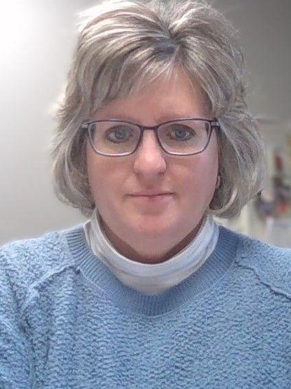 A woman wearing glasses and a blue sweater is taking a selfie.