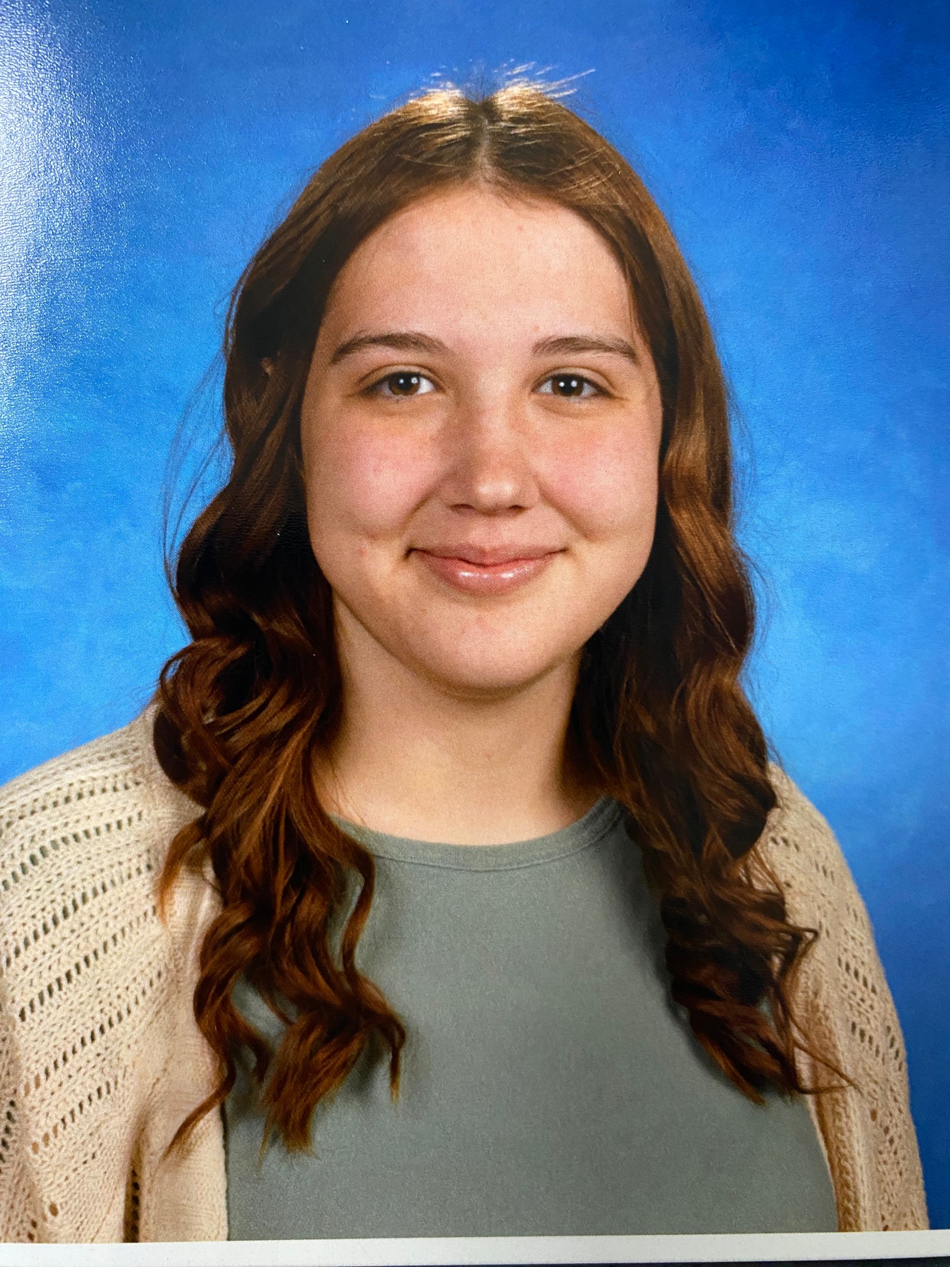 A young woman is posing for a picture in front of a blue background.