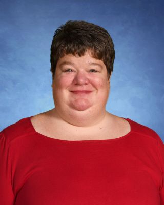 A woman in a red shirt is smiling in front of a blue background.