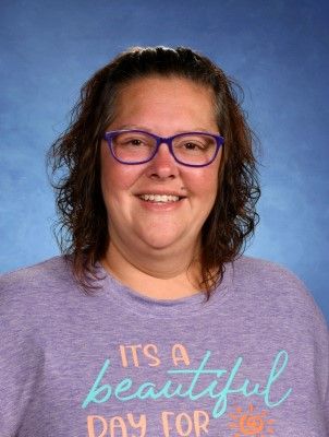 A woman wearing glasses and a purple shirt is smiling for the camera. This is Natasha Mosher.