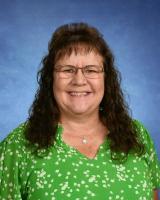 A woman wearing glasses and a green shirt is smiling for the camera.This is Kathy Roessner.