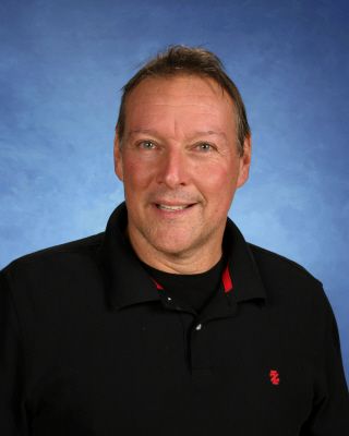 A man wearing a black shirt with a red emblem on it is smiling for the camera.