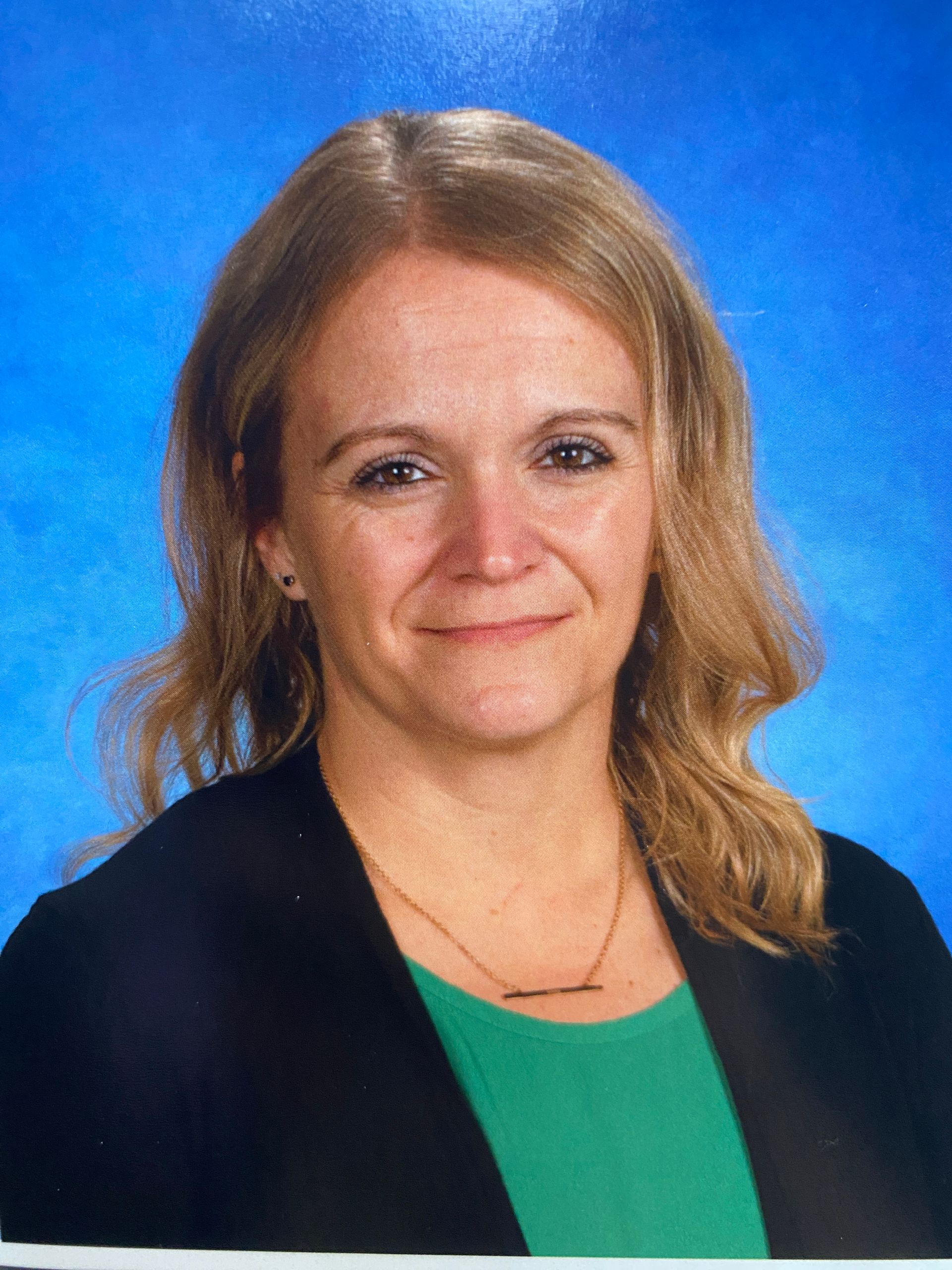 A woman in a green shirt and black jacket is smiling for a picture.