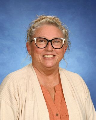 A woman wearing glasses and a sweater is smiling for a picture. This is Marty Sheets.