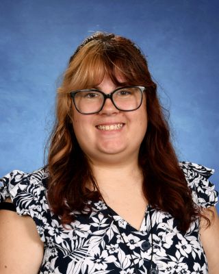 A woman wearing glasses and a floral shirt is smiling for a picture.