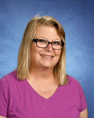 A woman wearing glasses and a purple shirt is smiling for the camera.