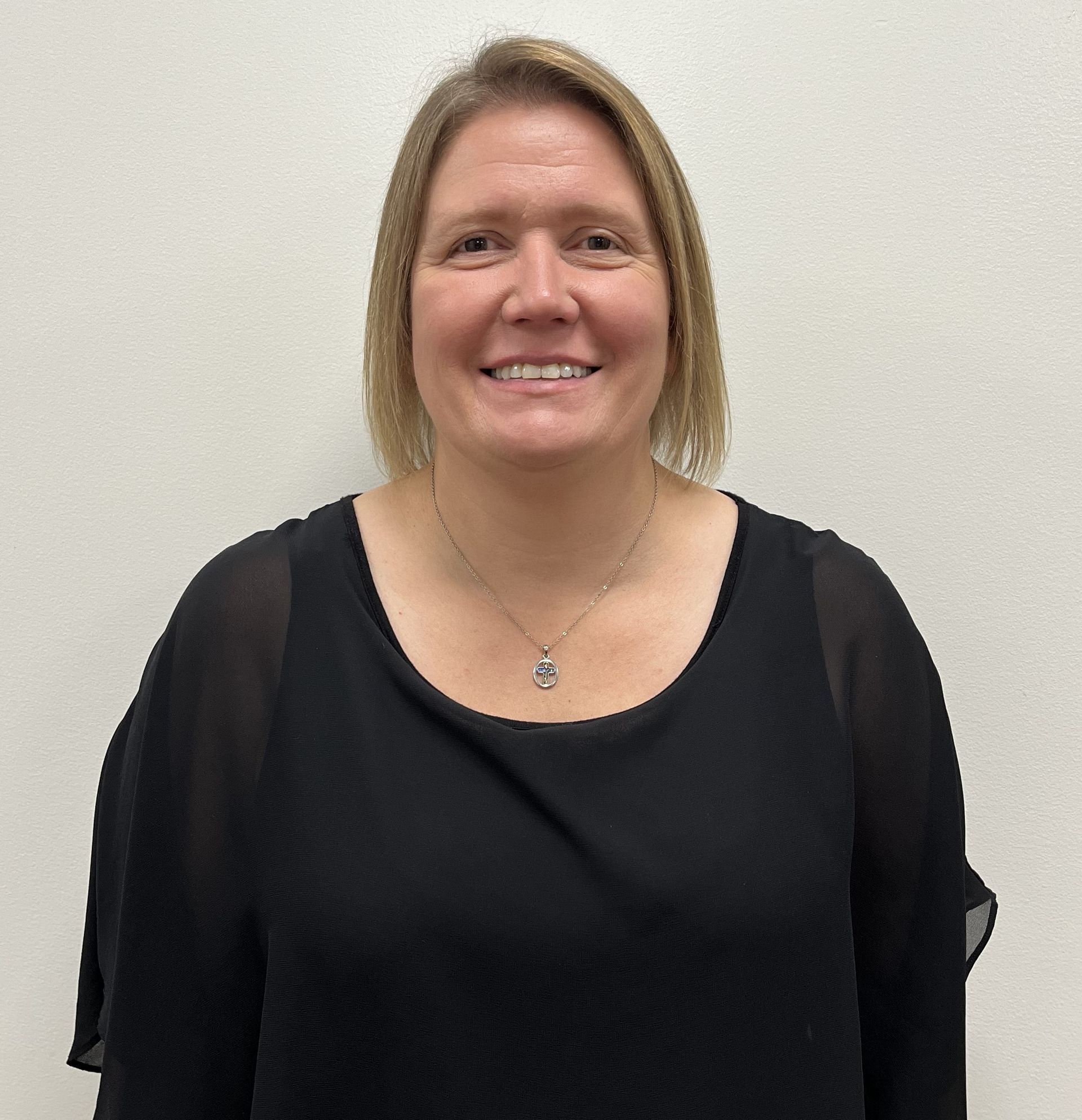 A woman wearing a black shirt and a necklace is smiling for the camera.