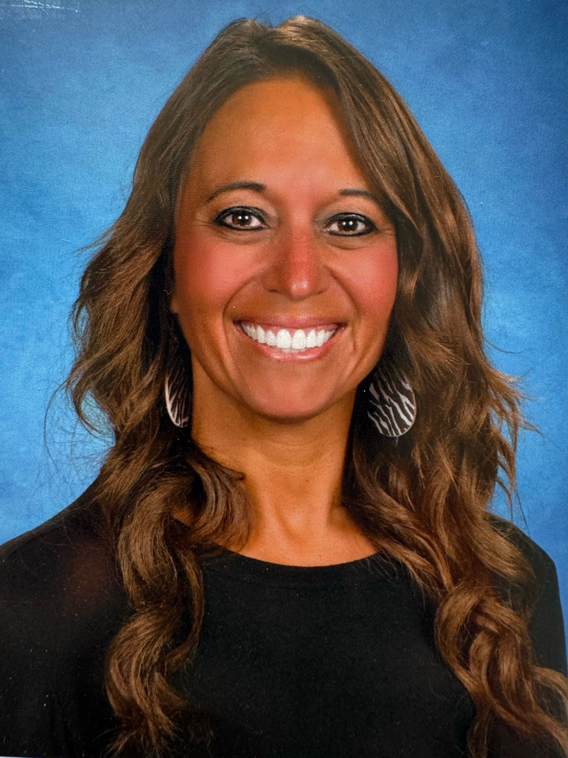 A woman with long brown hair is smiling in front of a blue background.