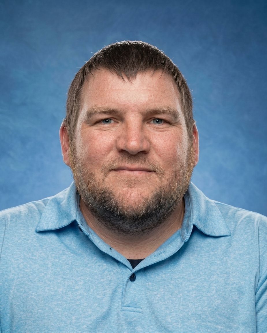 A man with a beard is wearing a blue shirt and smiling.