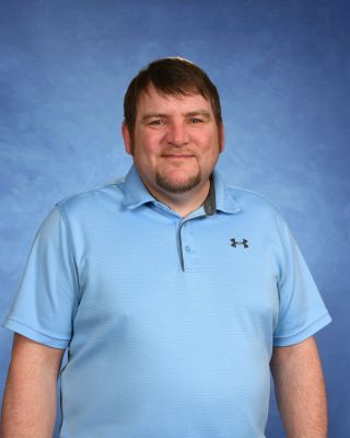 A man with a beard is wearing a blue shirt and smiling.