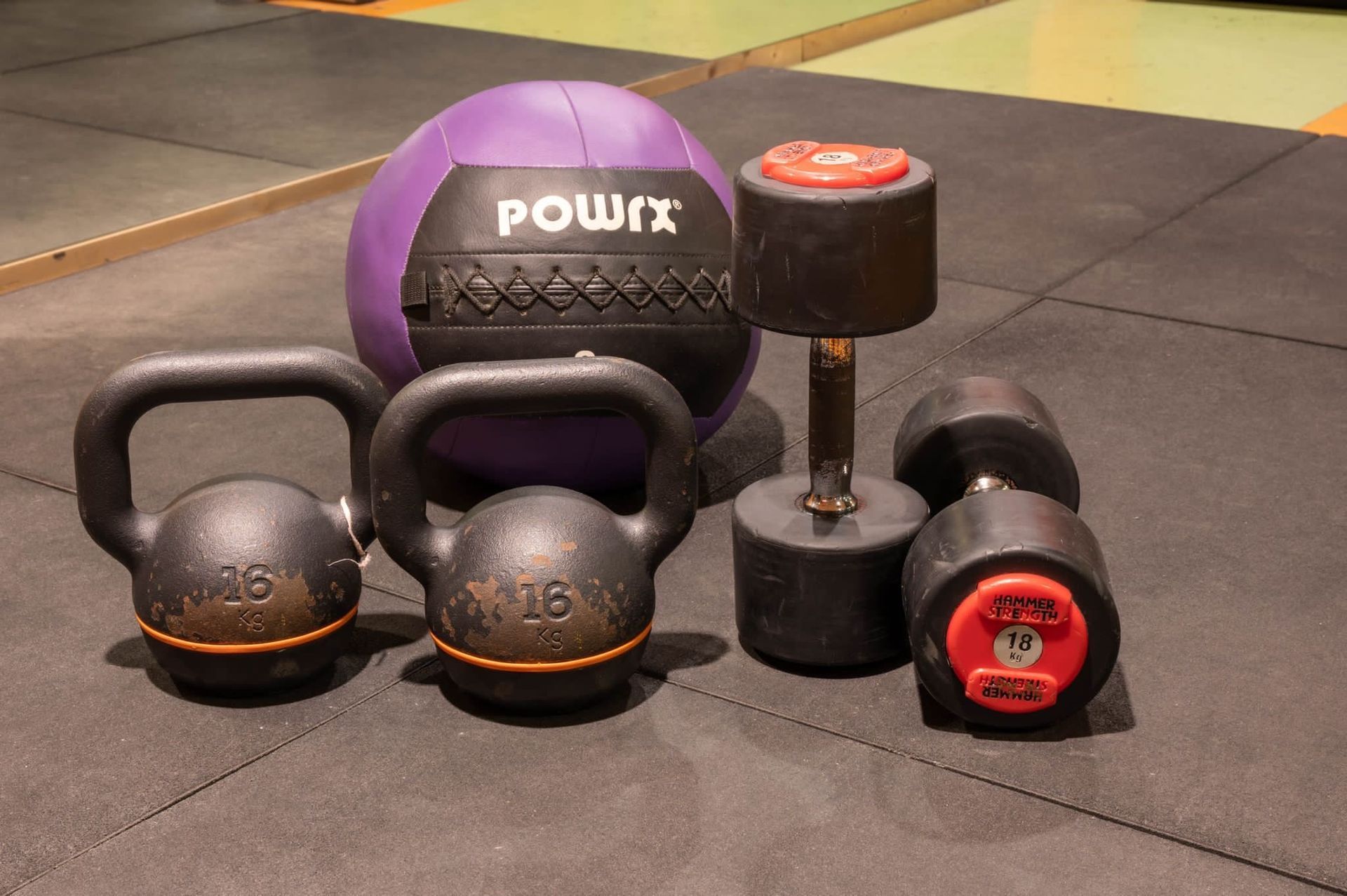 Vari attrezzi per l'allenamento: kettlebell, manubri, una palla medica e una ruota.