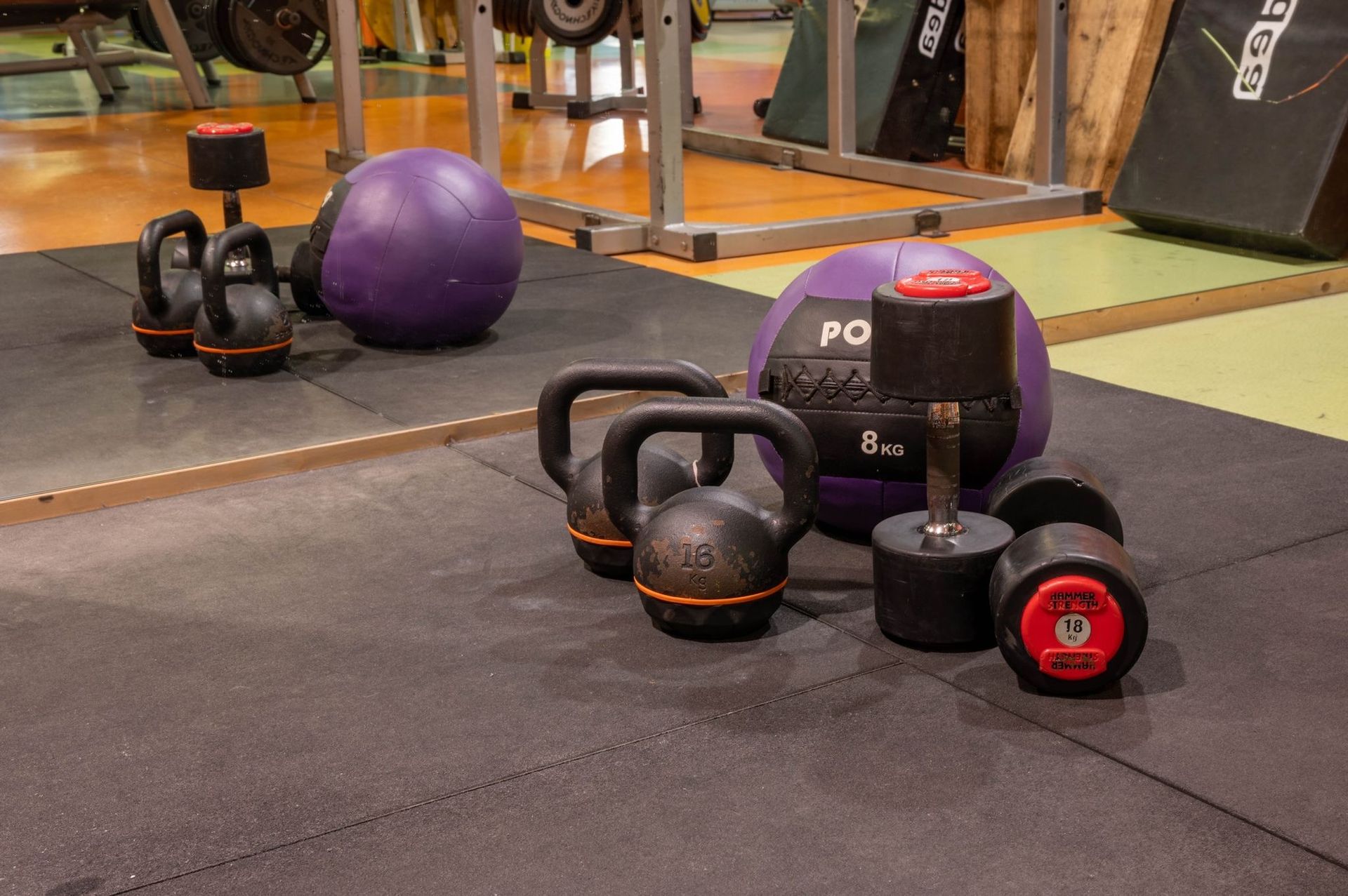 Un assortimento di kettlebell e una palla da ginnastica viola sul pavimento di una palestra.