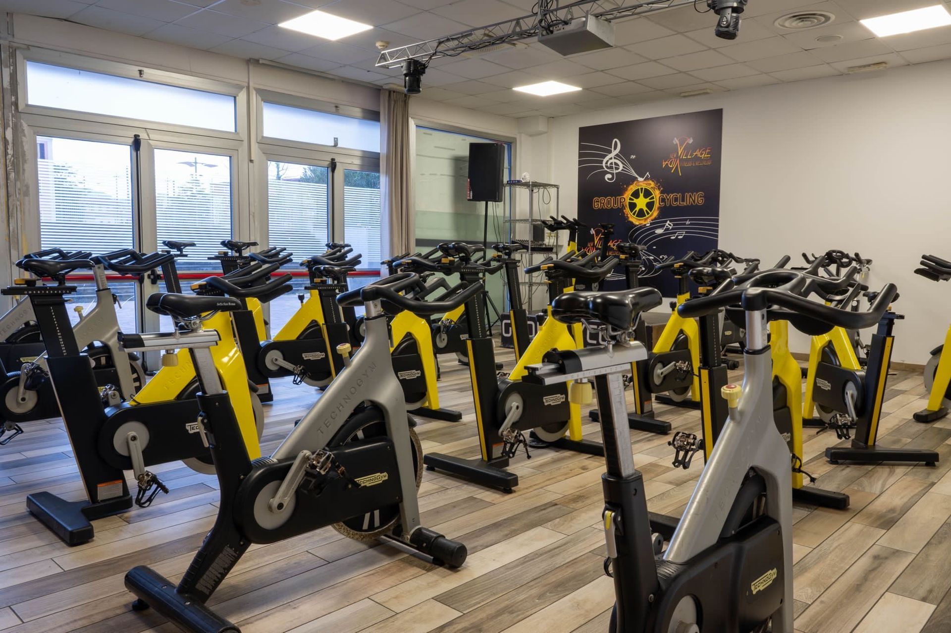 Sala per spinning indoor con file di cyclette nere e gialle sotto finestre luminose