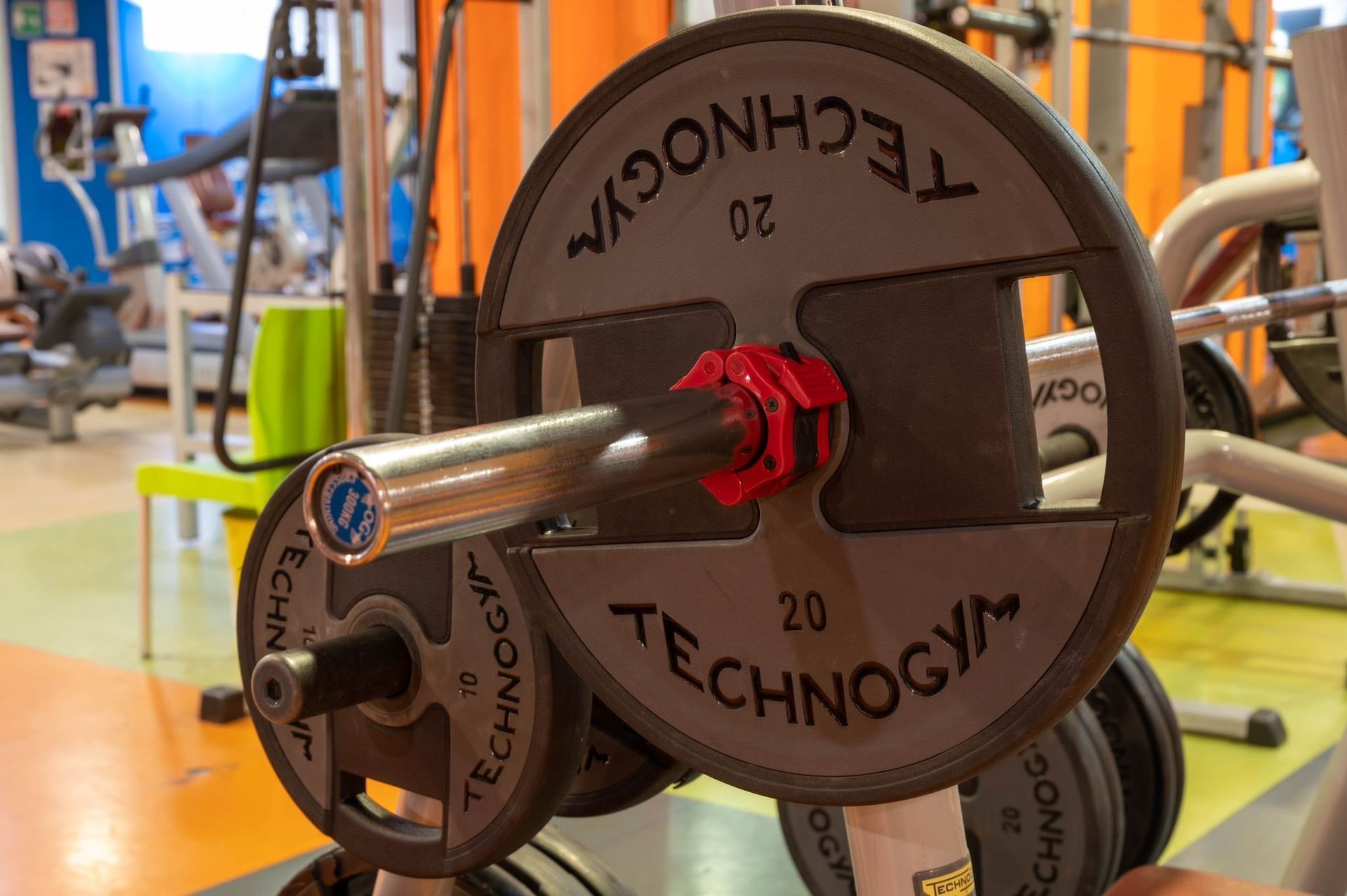 Primo piano della maniglia di una macchina per pesi Technogym in una palestra, con attrezzature sfocate sullo sfondo.