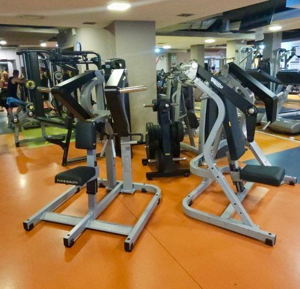 Pavimento della palestra con due macchine per esercizi grigie su un tappetino di gomma arancione.