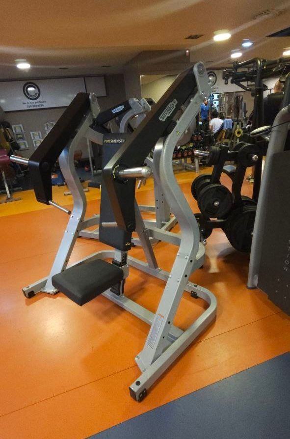 Due macchine per esercizi argentate in una palestra con pavimento e specchi arancioni
