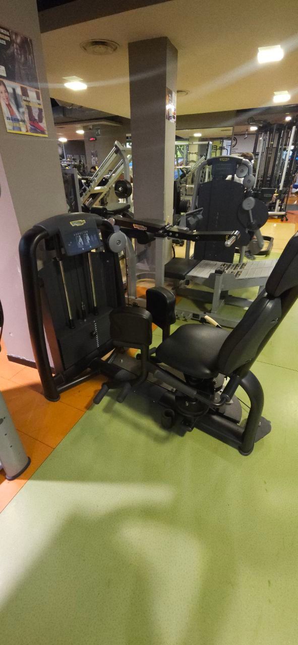 Macchina per pesi da palestra con sedile e maniglie imbottiti neri su pavimento verde.