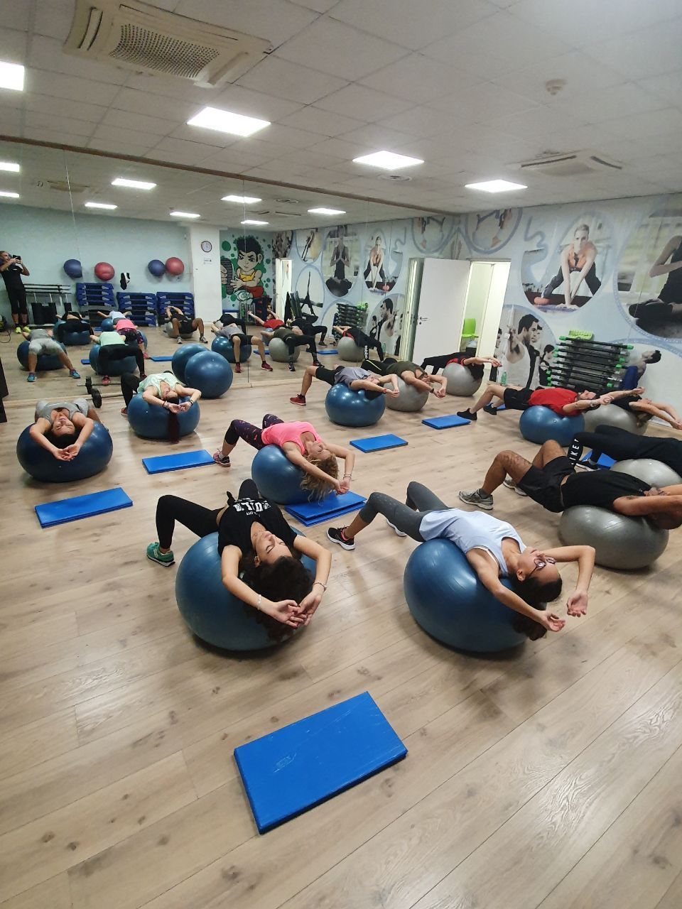 Persone che si allenano su palle da fitness in una palestra con pareti a specchio.