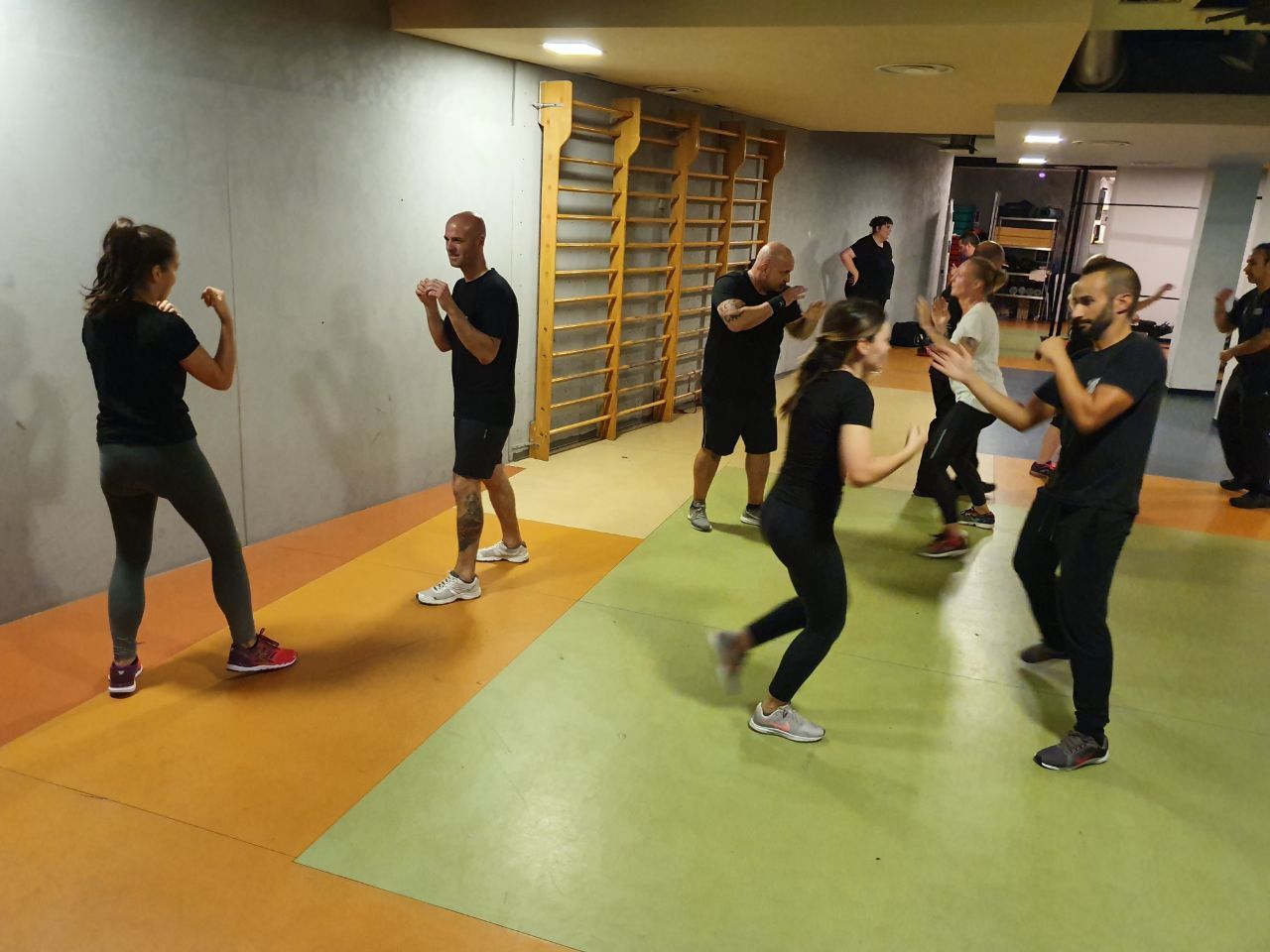 Persone che praticano arti marziali in una sala di allenamento con tappetini arancioni e verdi.