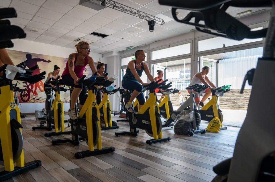 Persone che si allenano su cyclette in una luminosa sala spinning al coperto.