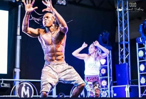 Un artista a torso nudo balla sul palco sotto luci blu, con una donna in posa alle sue spalle.