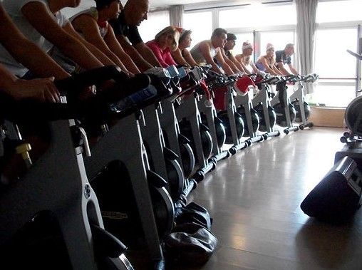 Persone su cyclette in una luminosa sala per lezioni di spinning al coperto.