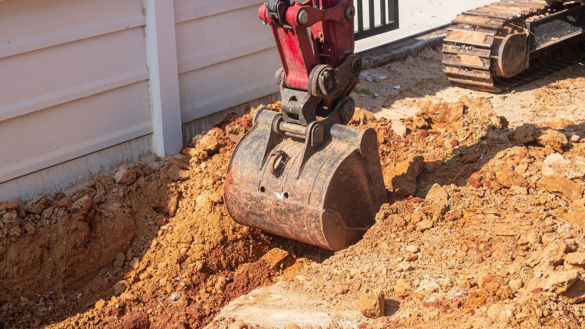 Excavator bucket digging into dirt beside a house foundation site Excavator bucket digging into dirt beside a house foundation site
