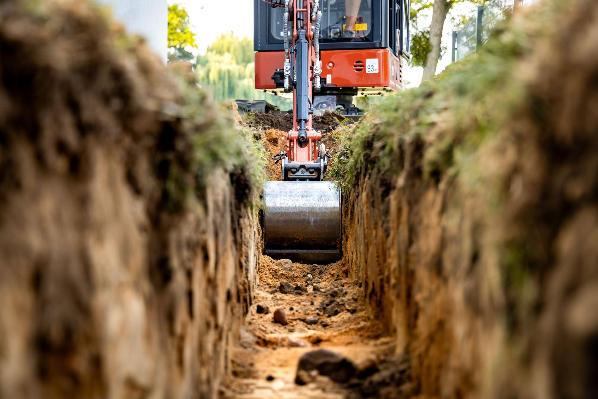 Excavator digging a trench, with a dirt wall on both sides and the bucket centered in view Excavator digging a trench, with a dirt wall on both sides and the bucket centered in view
