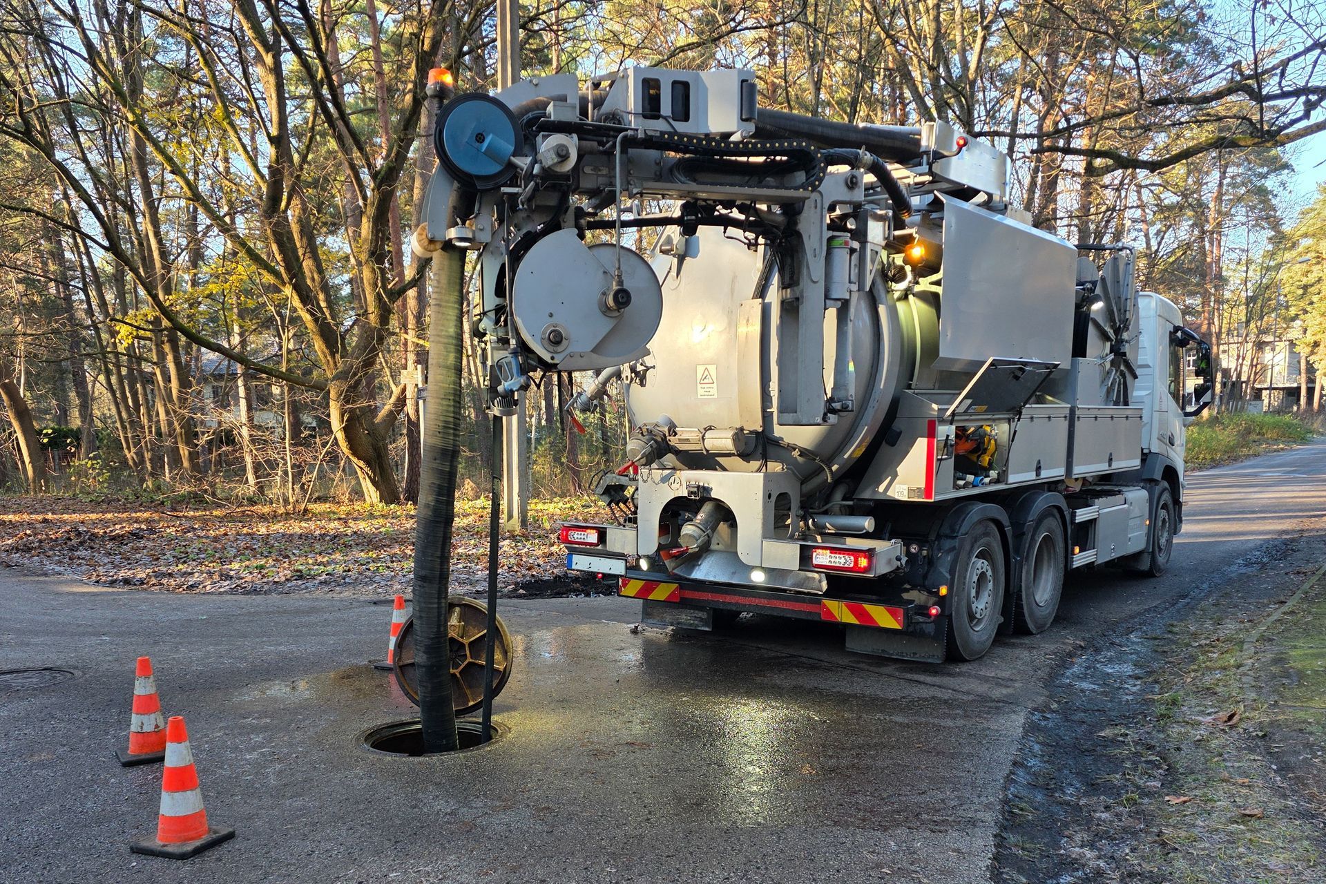 Utility truck with large drilling rig on a wet road beside orange cones in a wooded area Utility truck with large drilling rig on a wet road beside orange cones in a wooded area
