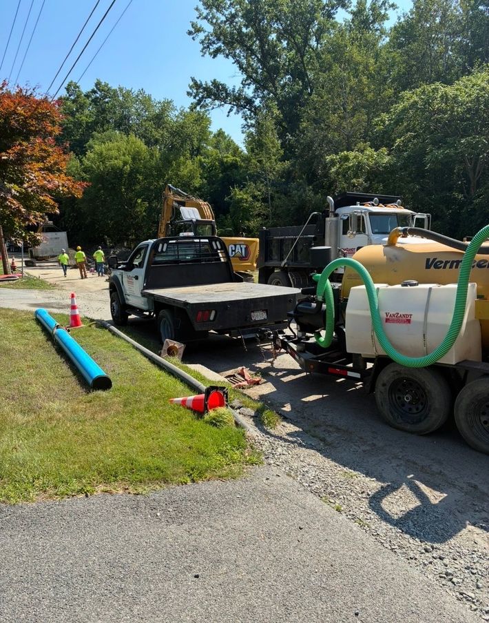 Construction trucks and equipment lined up on a driveway beside a grassy yard and trees. Construction trucks and equipment lined up on a driveway beside a grassy yard and trees.
