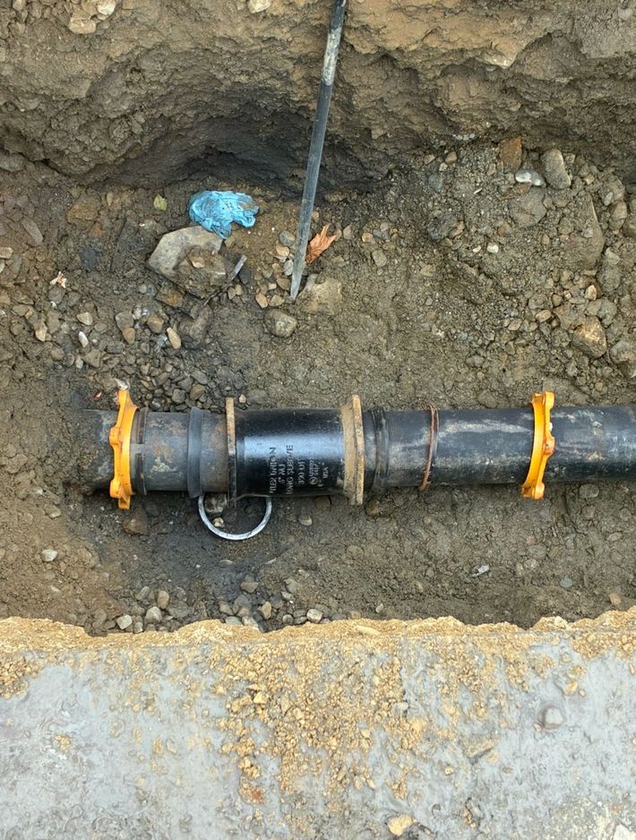 Black pipe joint in a dirt trench, secured with orange clamps and a metal ring. Black pipe joint in a dirt trench, secured with orange clamps and a metal ring.