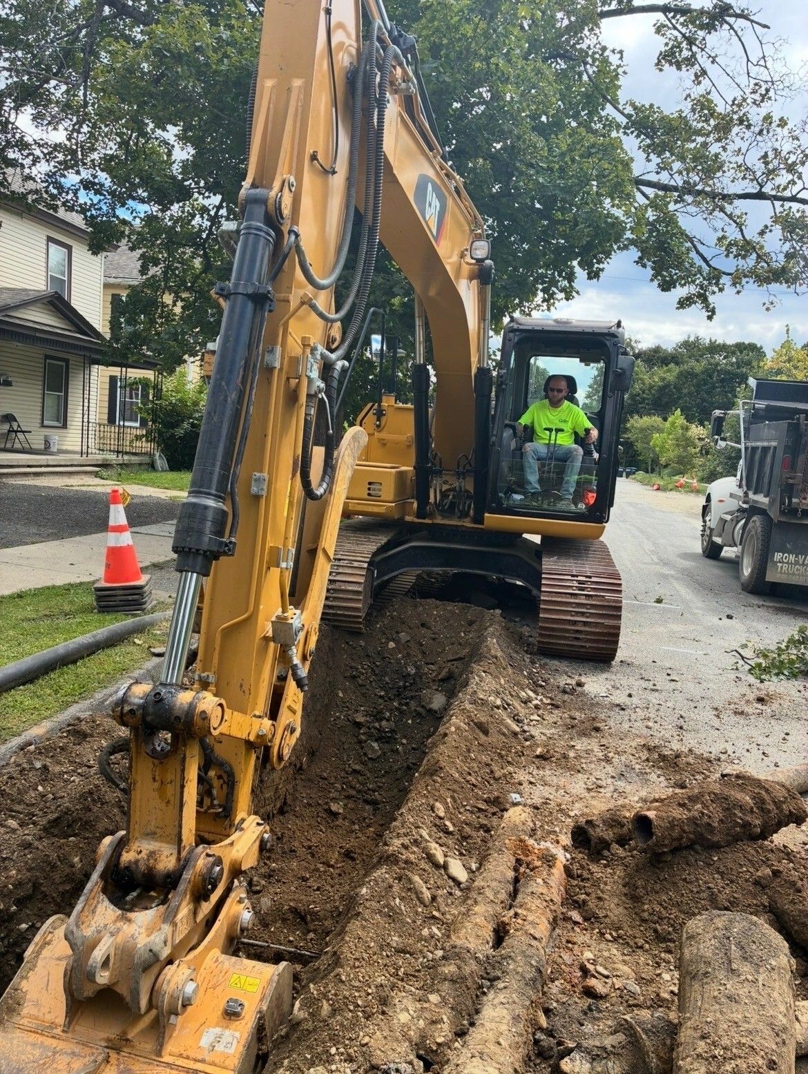 Yellow excavator digging a trench on a residential street beside a house and traffic cone Yellow excavator digging a trench on a residential street beside a house and traffic cone