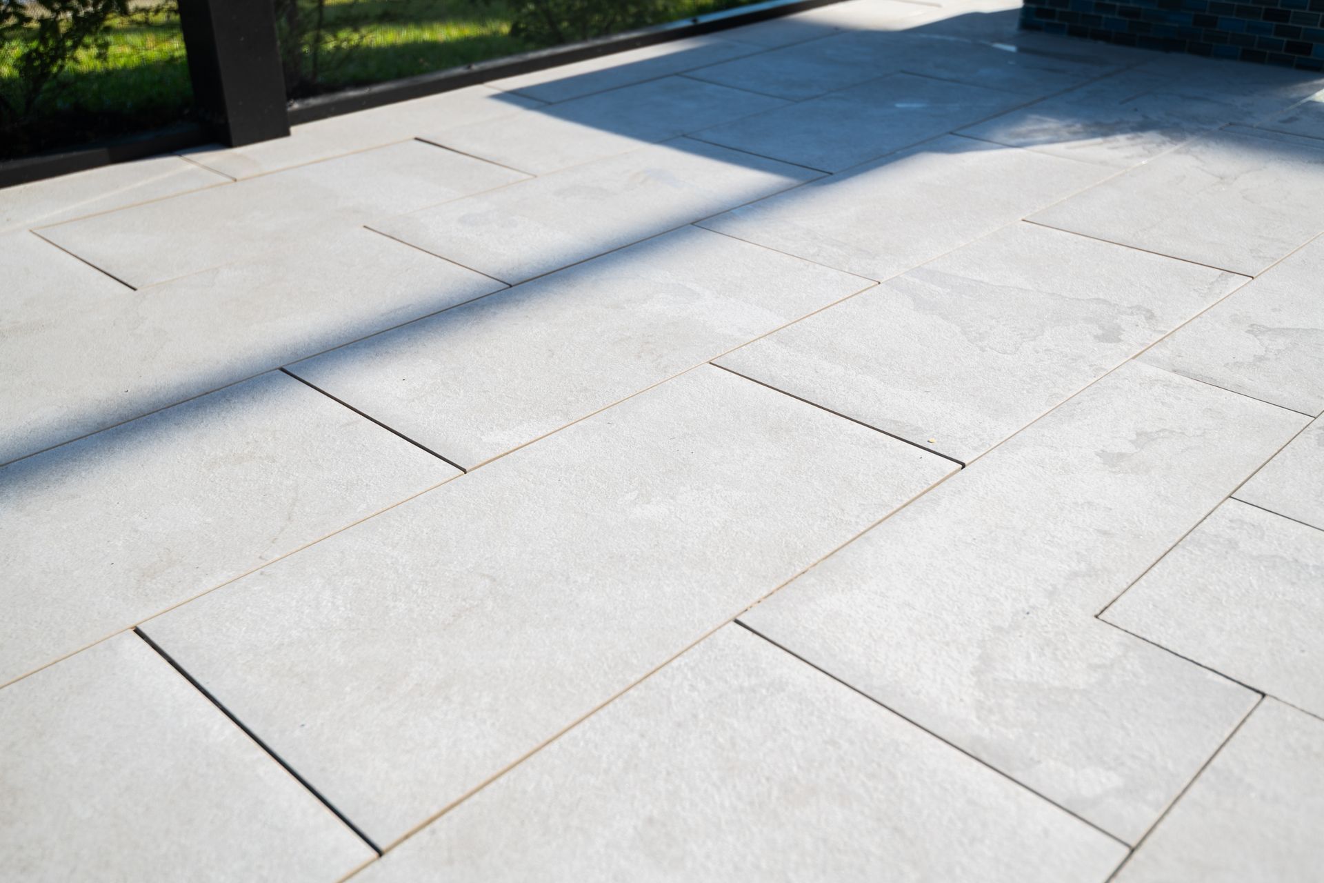 Light gray stone patio slabs in a sunny outdoor setting, with grass at the edge