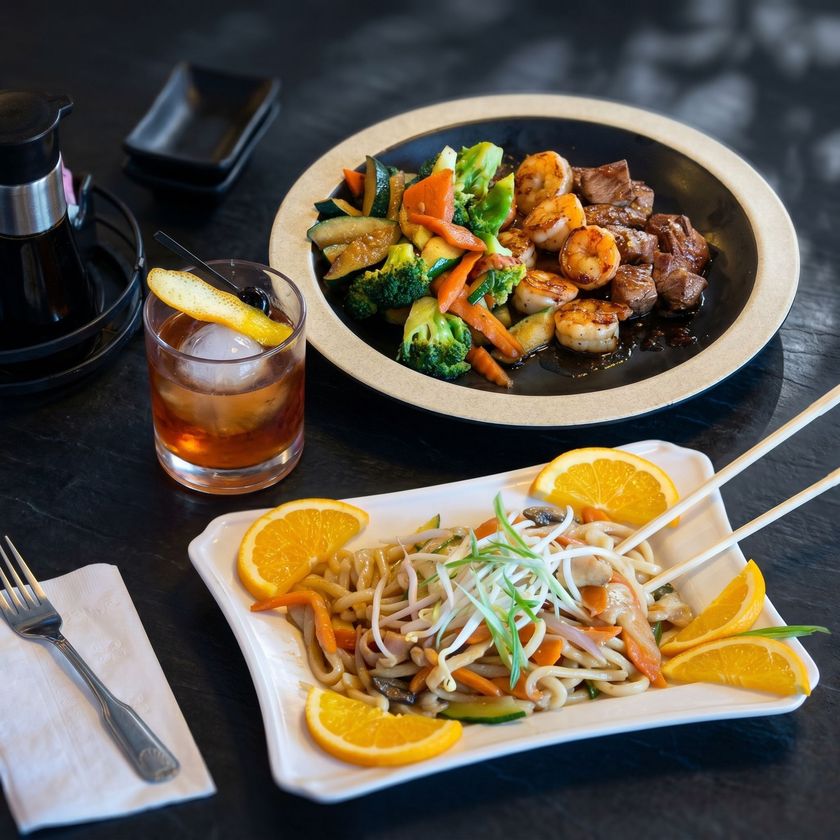 Asian meal with stir-fry, steak, and noodle dish garnished with orange slices on a table