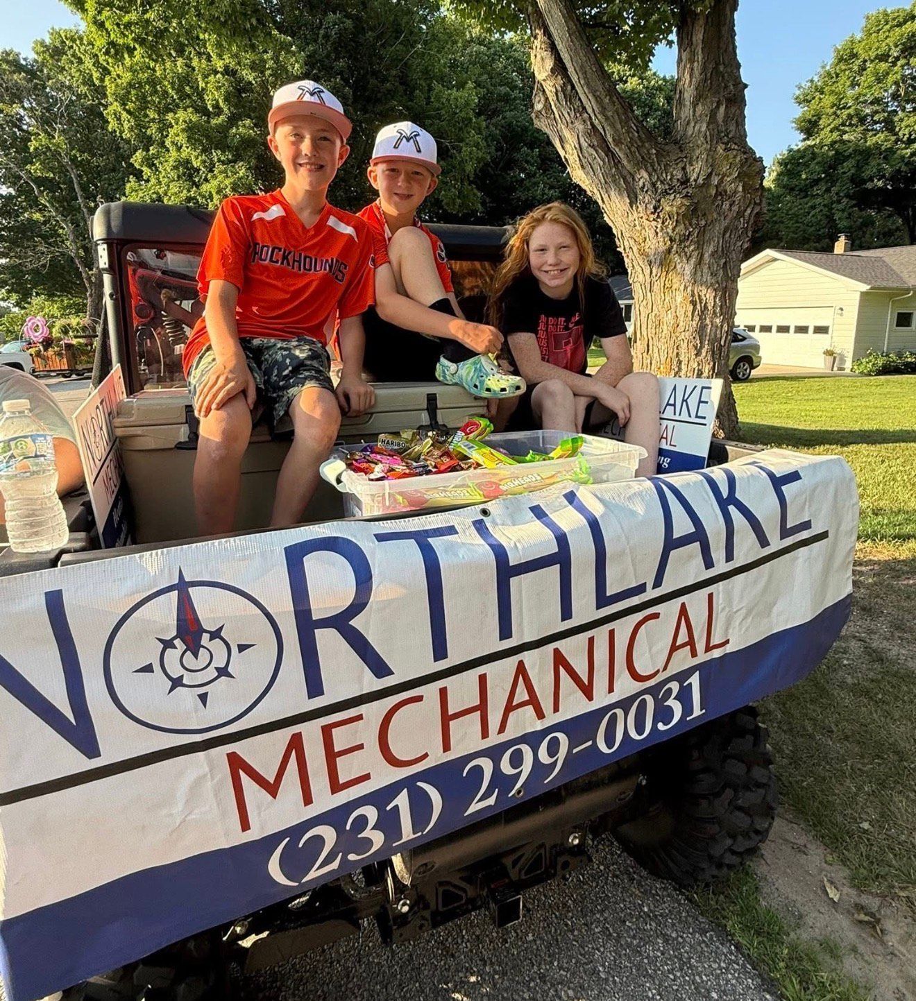 Three children sit on a Northlane Mechanical truck parade float outdoors.
