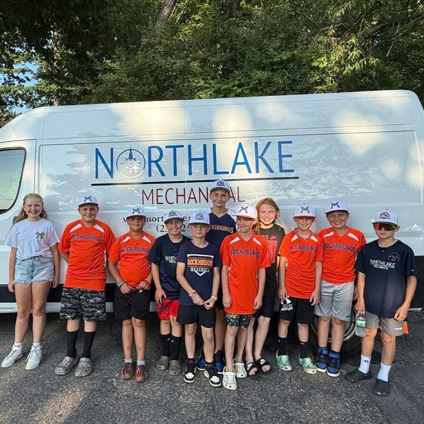Group of children in orange and navy shirts posing beside a Northlake Mechanical van outdoors