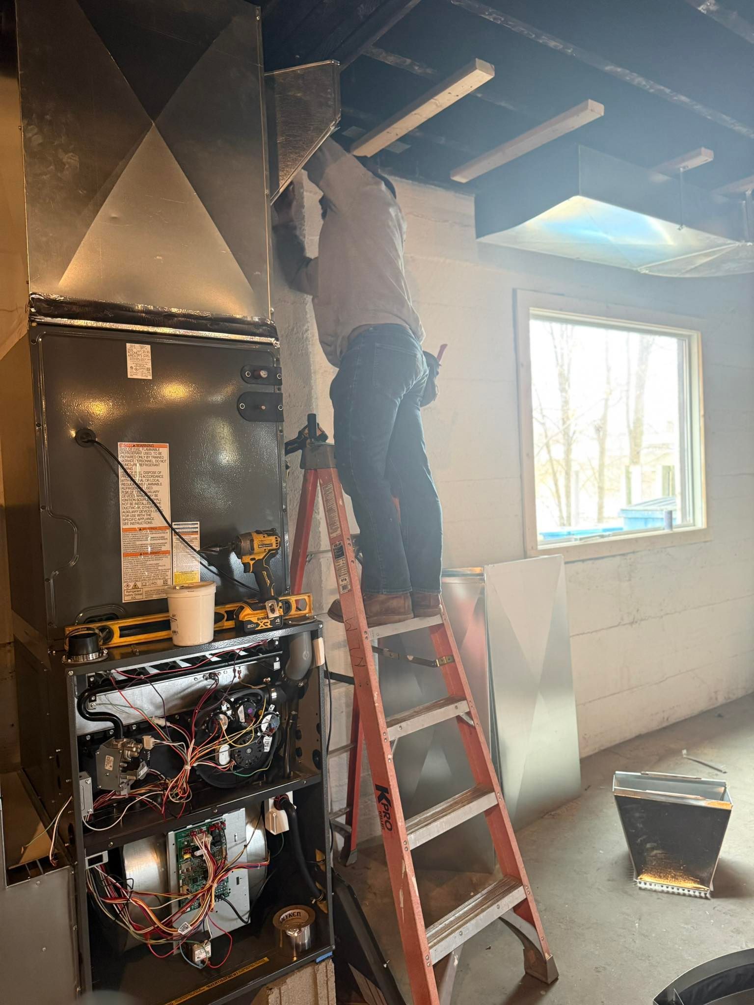Person on a ladder repairing a damaged kitchen ceiling amid exposed wiring and debris.