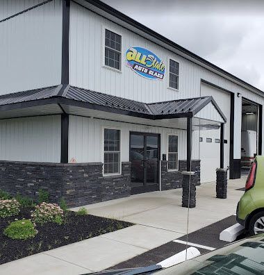 All-Star Auto Body shop exterior, white building with black trim, sign, and garage doors. Green car parked.