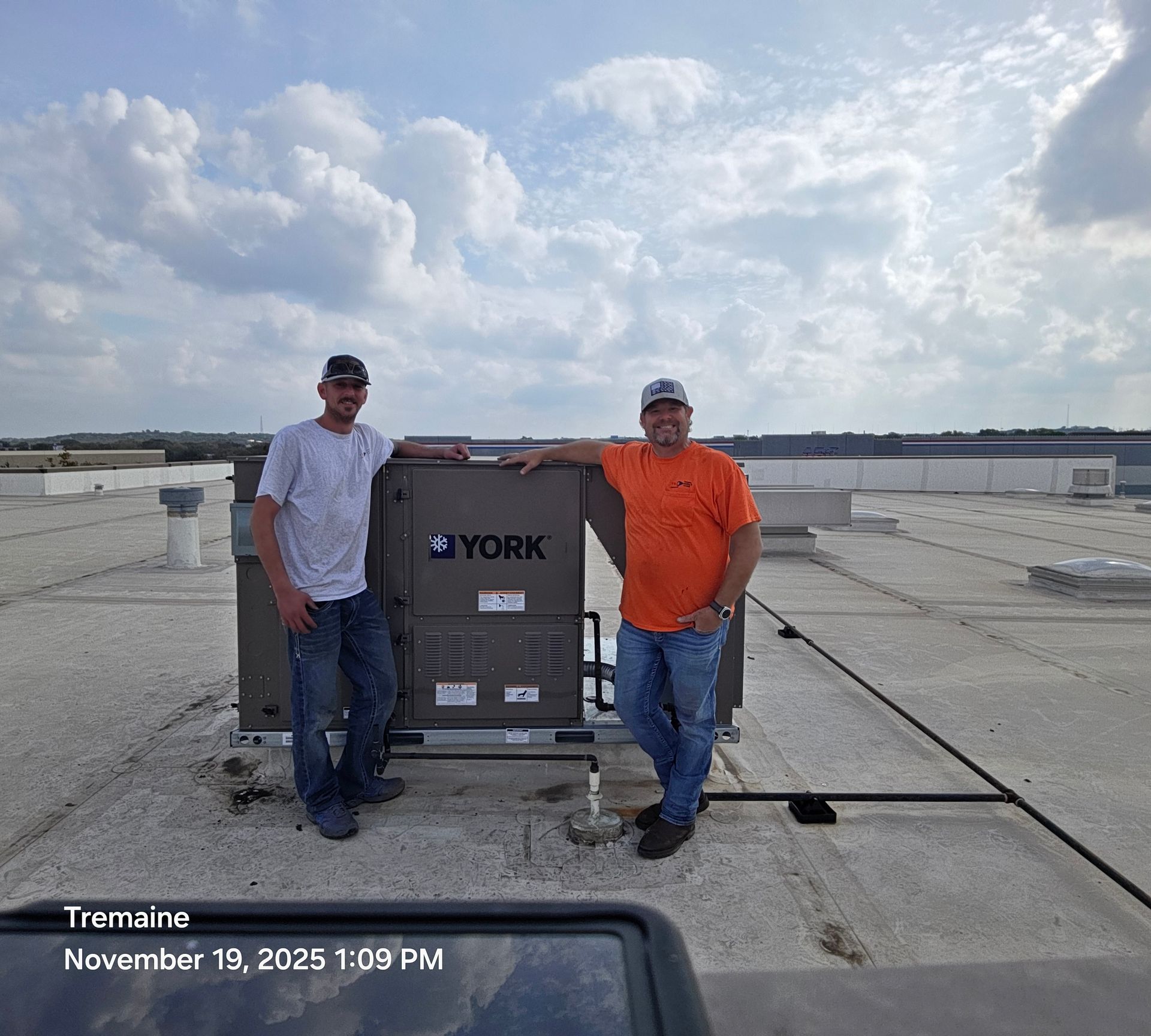 Two men stand beside a York rooftop HVAC unit on a flat roof under a cloudy sky.