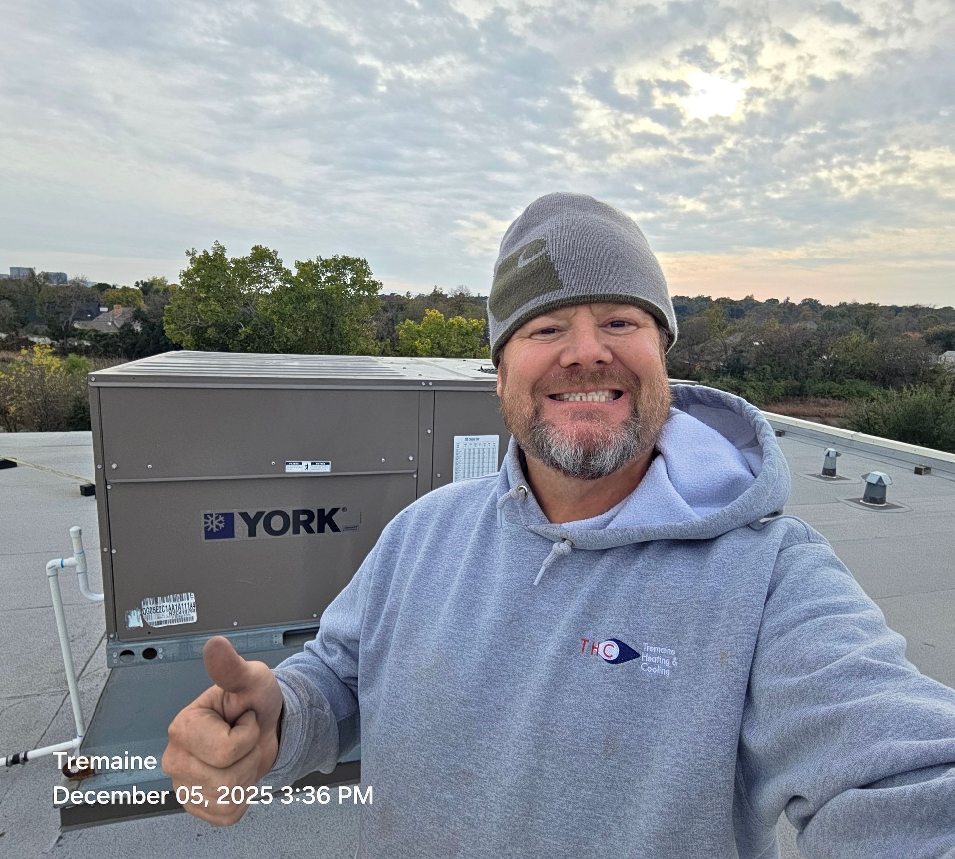 Man on a rooftop smiles, giving a thumbs up near a York HVAC unit. Overcast sky.