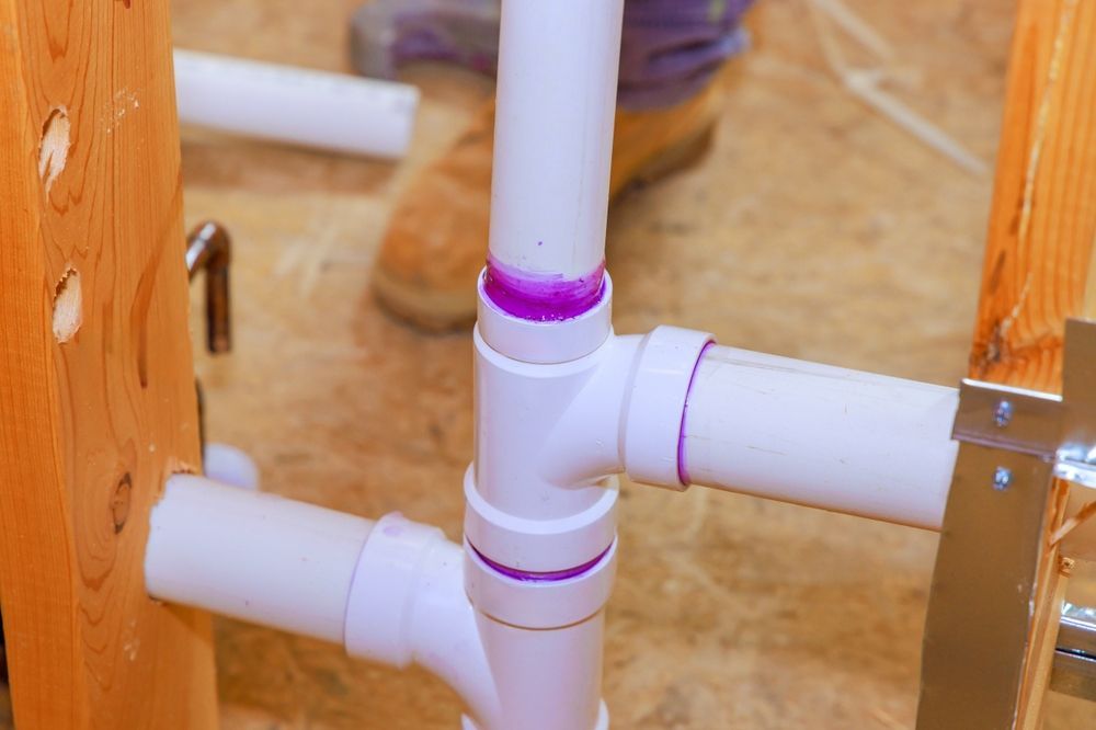 White PVC plumbing pipes with purple primer are joined together in a wooden frame.