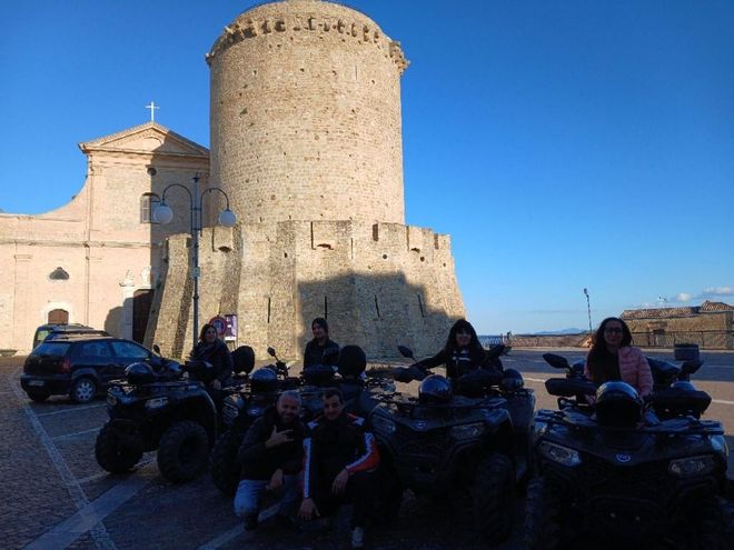 ATVs parked in a stone courtyard beside an old castle tower under a clear blue sky