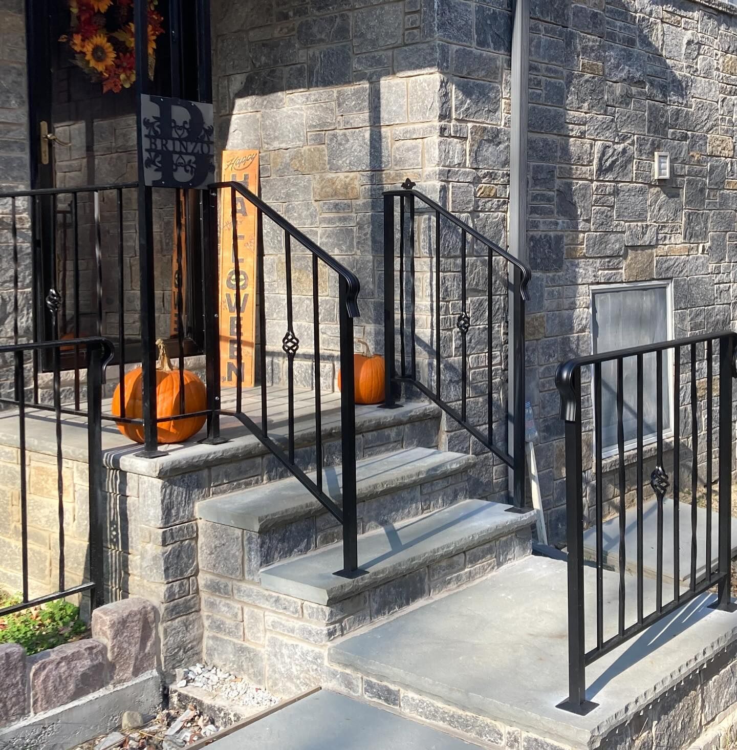 A stone front porch features black metal railings, a wooden 