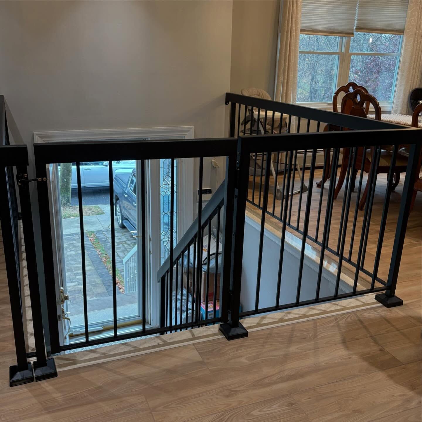 A black metal safety gate and railing installed at the top of a staircase, situated on wood-look flooring.